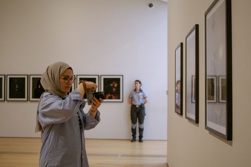 Free A woman takes pictures in an art gallery, focusing on framed paintings. Stock Photo