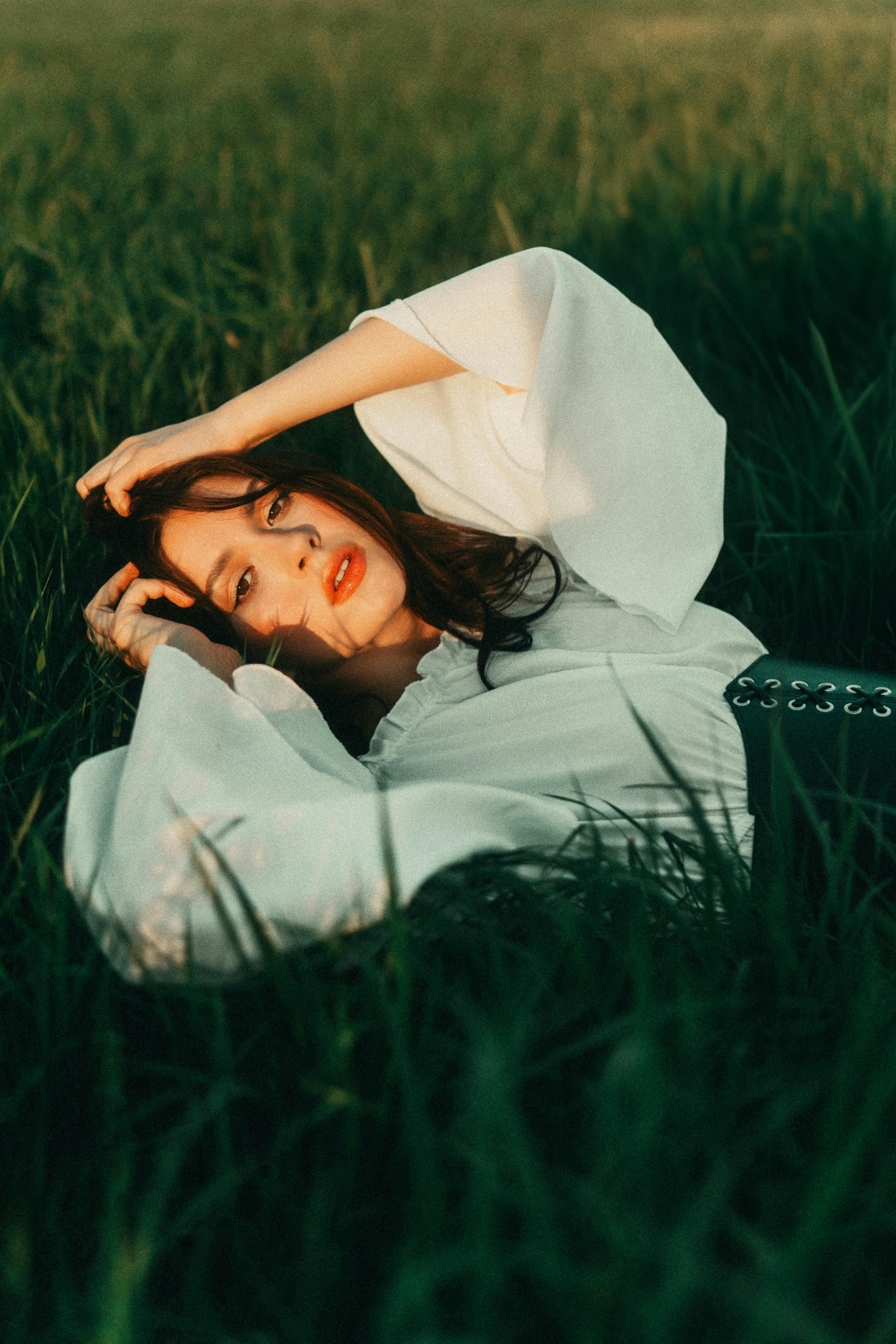 Free Young Brunette Woman in White Blouse and Corset Lying in Tall Grass Stock Photo