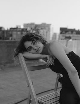 Artistic black and white portrait of a woman leaning on a chair on a city terrace, showcasing an urban vibe.