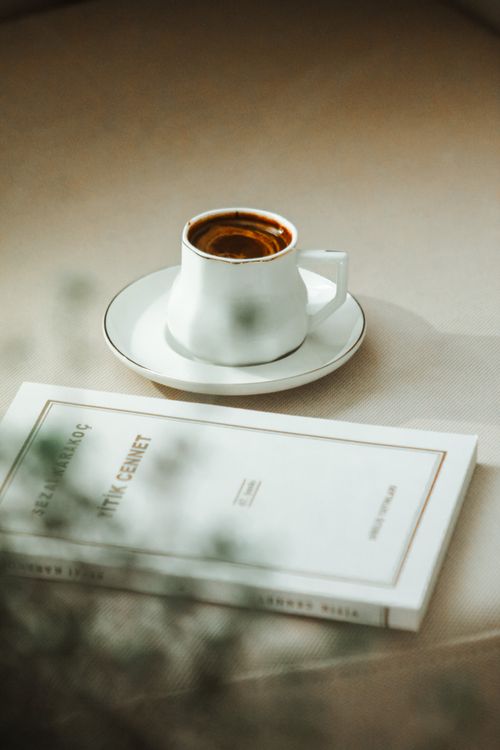 Free A serene still life with a cup of coffee and a book on a beige table, embodying calm and reflection. Stock Photo
