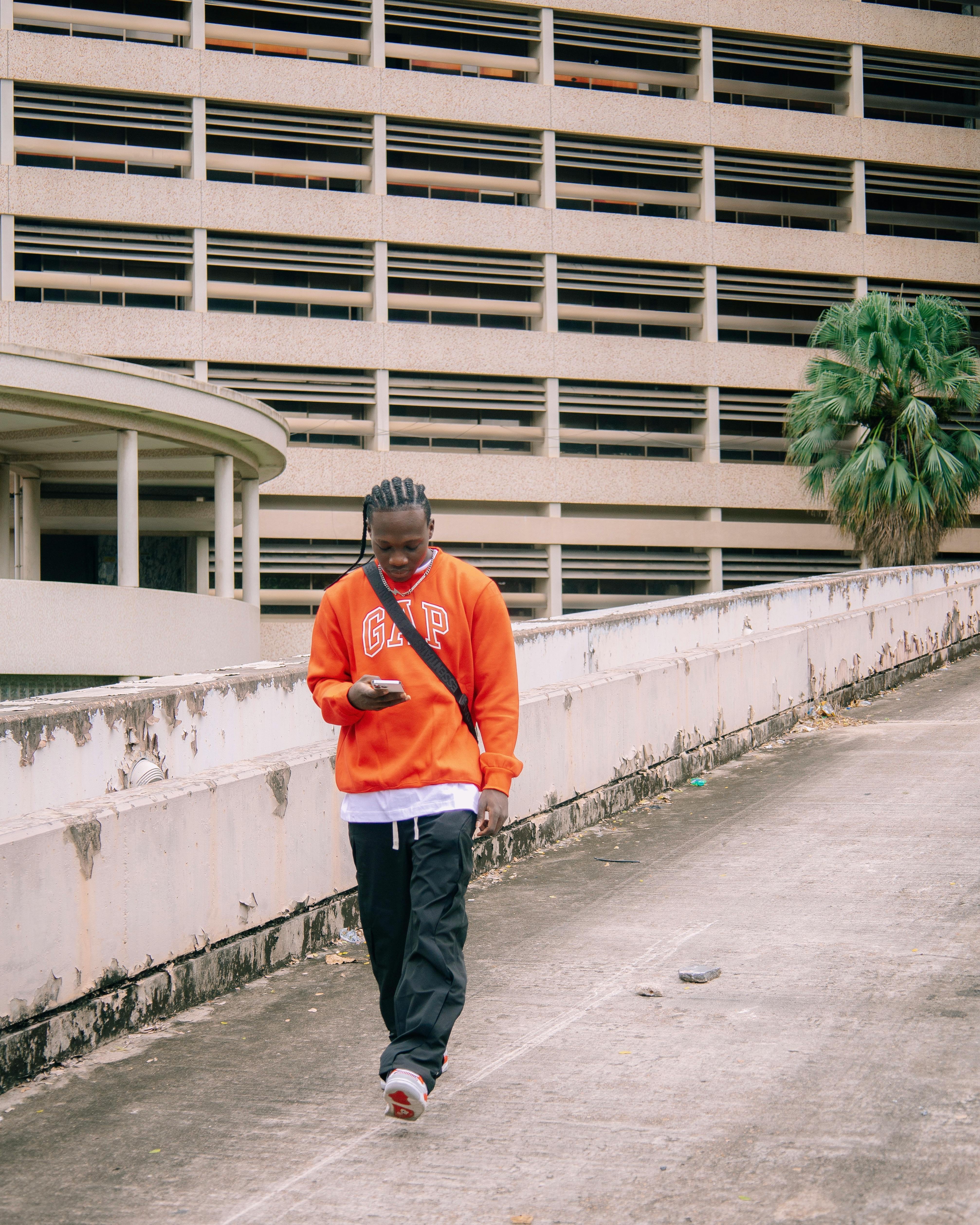 Urban scene of a young man walking with his cellphone in a city environment, wearing casual attire.