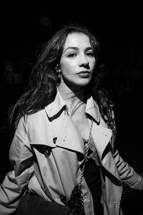 Black and White Portrait of a Young Woman in Trench Coat Standing on a Dark Street