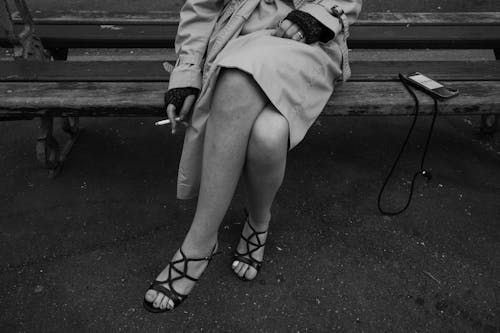 Black and White Photo of a Woman in Trench Coat Sitting on a Bench with a Cigarette