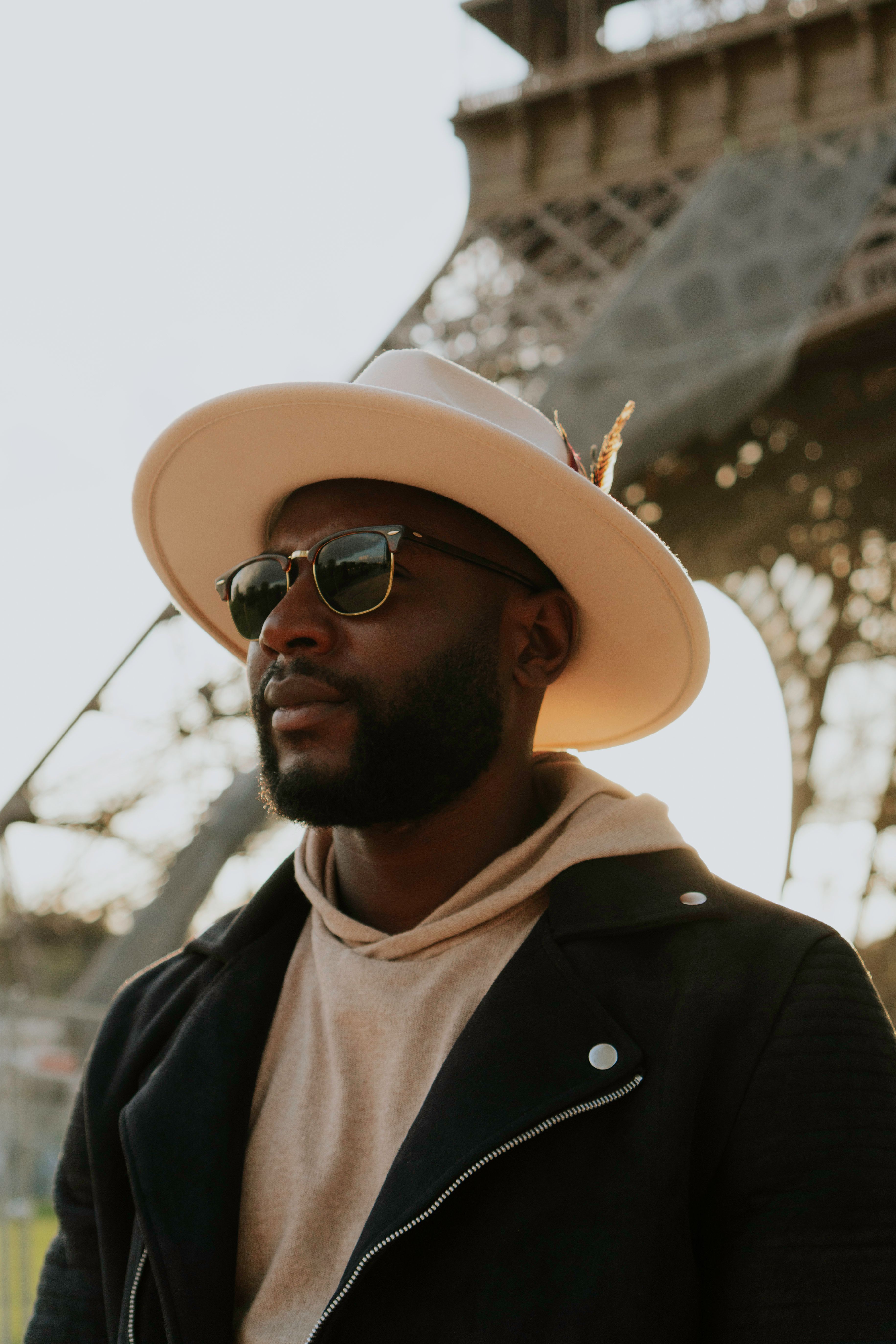 Fashionable man in hat and jacket posing by the Eiffel Tower in Paris at sunset.