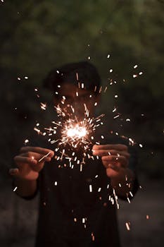 夜晚，一个人在户外手持烟花，绽放出明亮的火花，营造出节日气氛