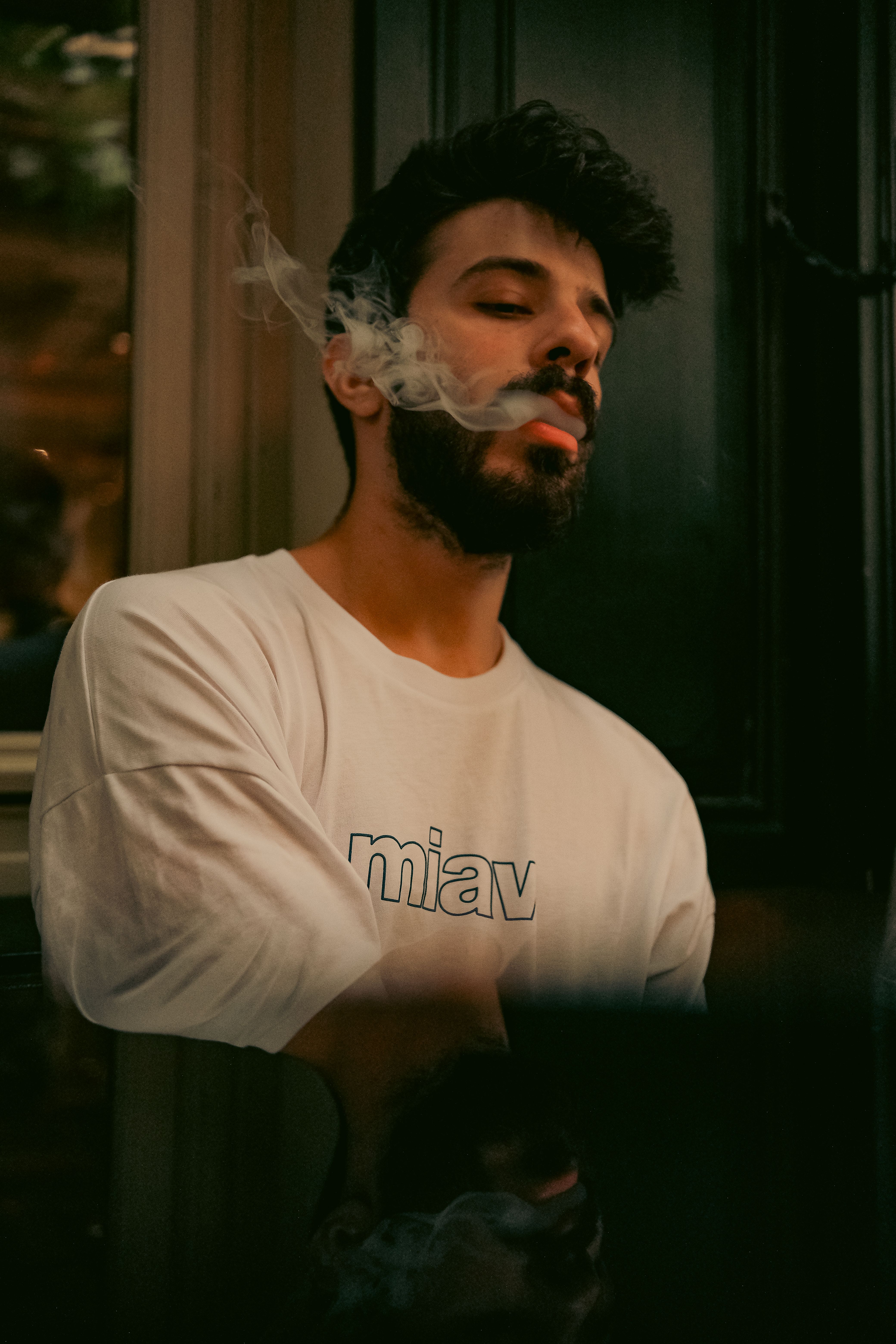 Portrait of a man exhaling smoke in a moody outdoor setting, capturing a serene moment.