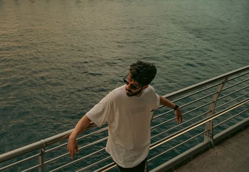 Man in sunglasses leans on a pier railing, overlooking the calm sea at sunset. Perfect for travel or lifestyle themes.