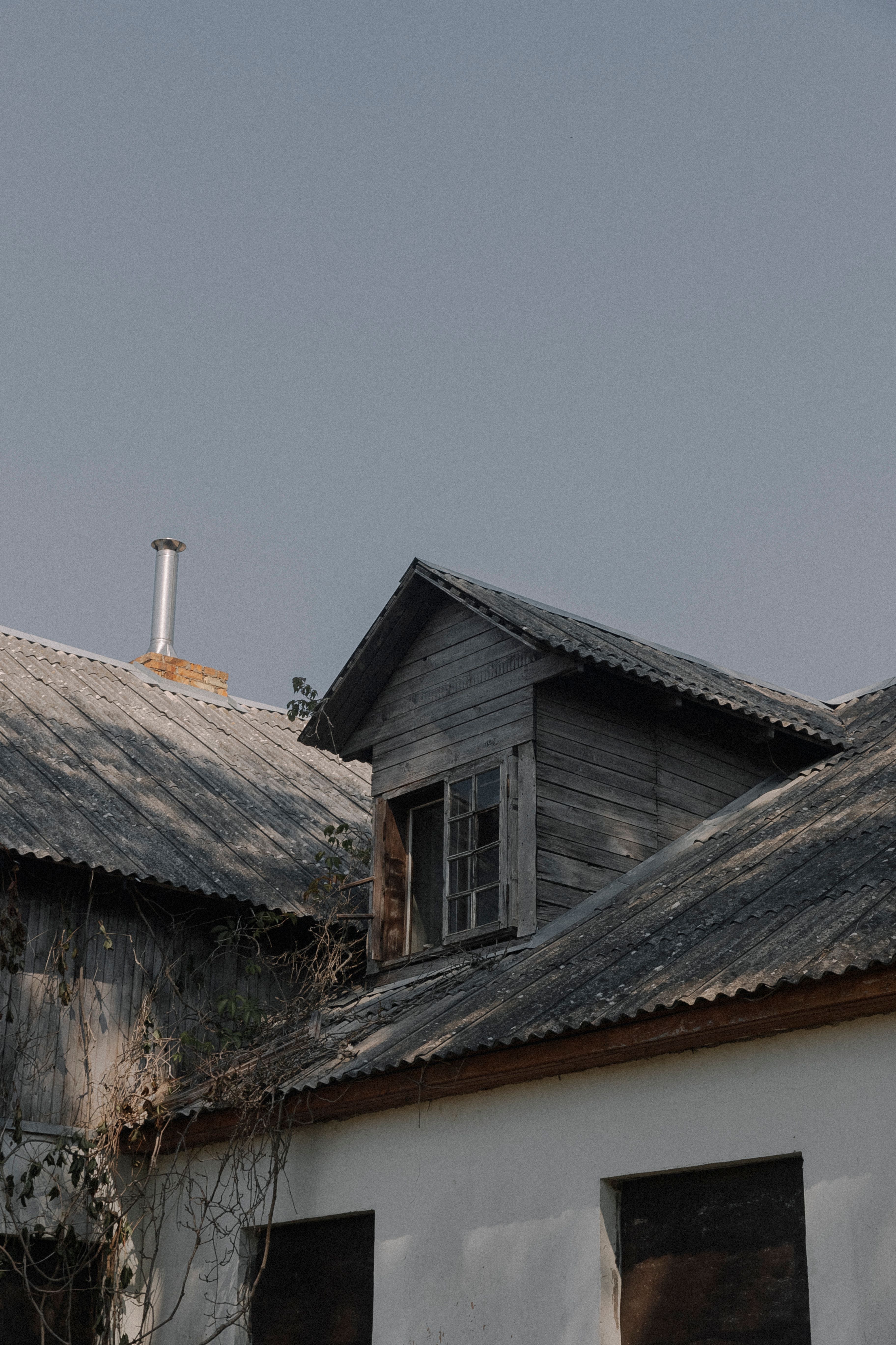 Quiet rustic farmhouse rooftop with corrugated metal in a rural setting under a cloudy sky.