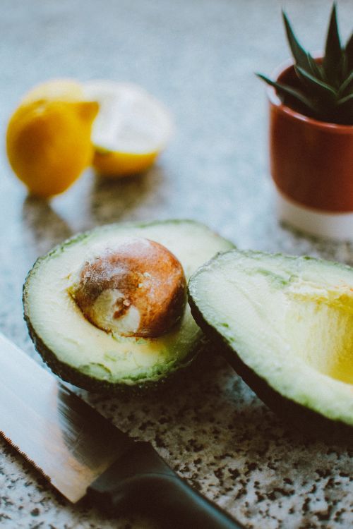 Free Close-up of a sliced avocado with knife, lemon and potted plant on a kitchen counter. Stock Photo