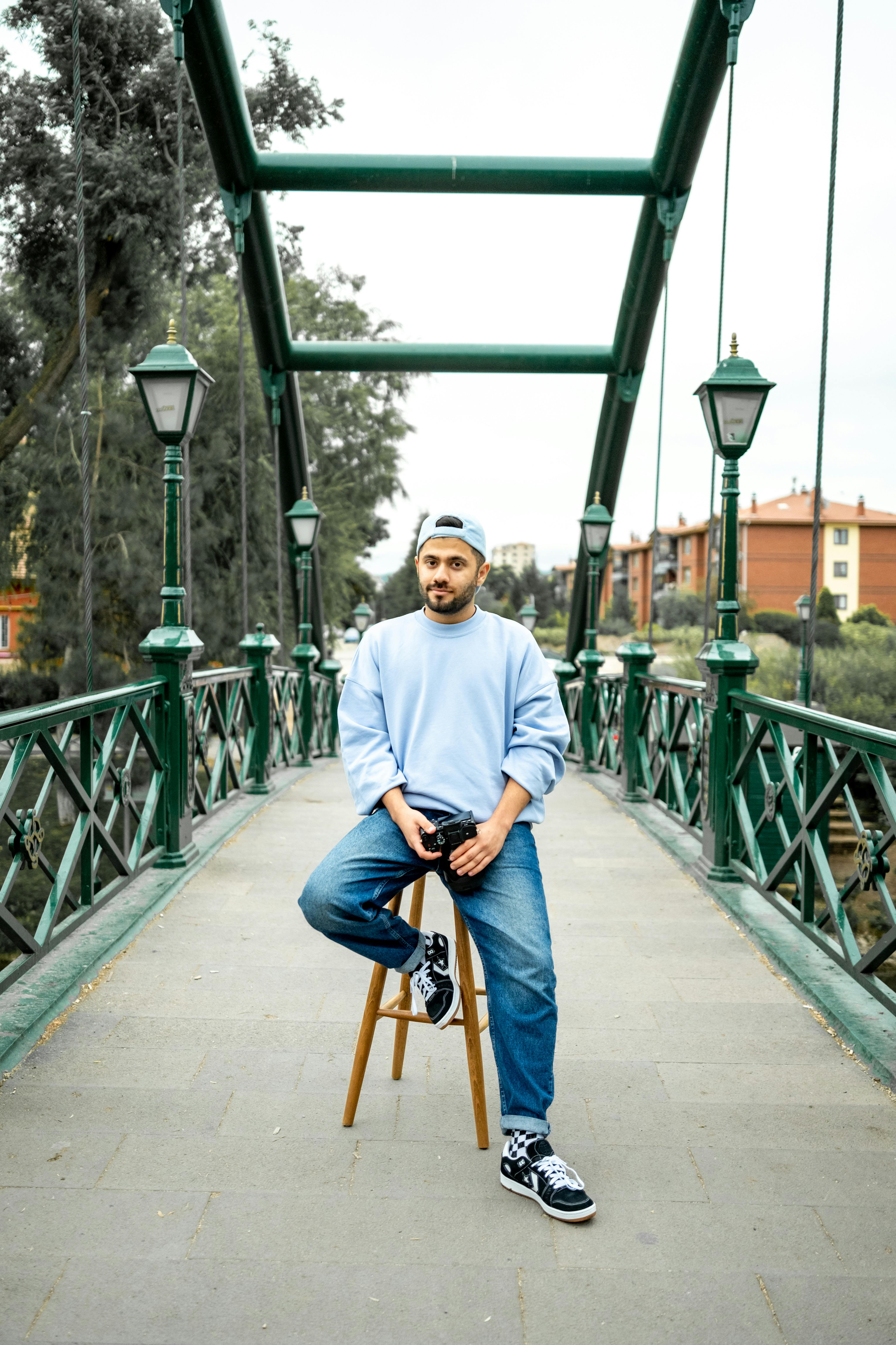 Man in blue sweatshirt sitting on stool on a stylish urban footbridge.