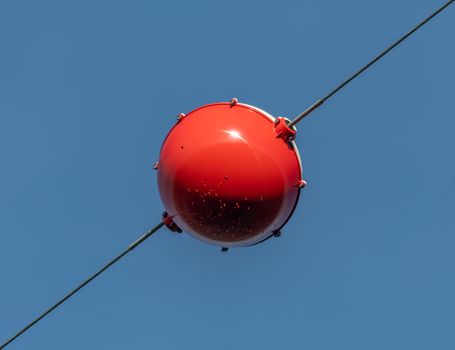 Close-up of a vibrant red aerial marker ball suspended on a wire against a clear blue sky.