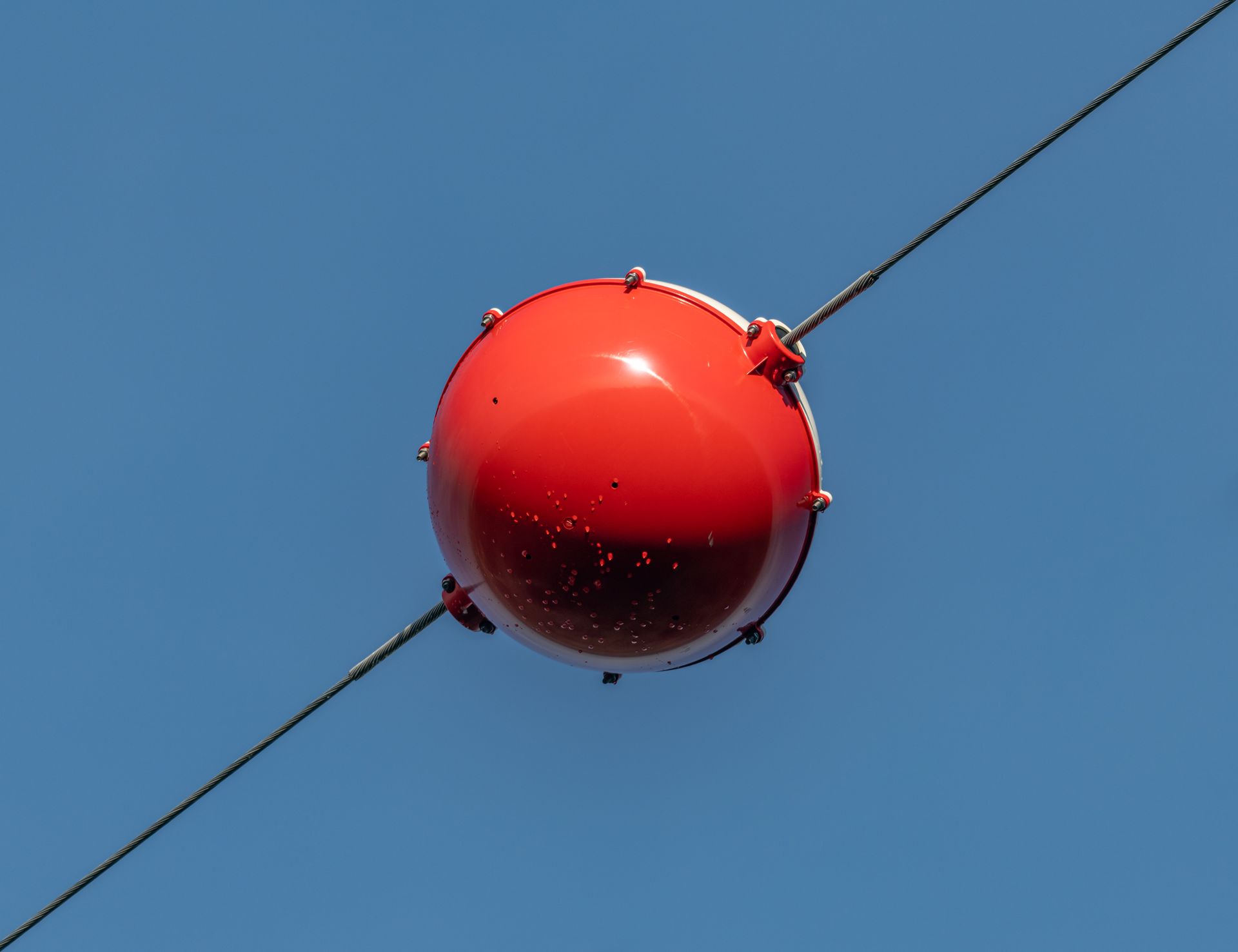 Close-up of a vibrant red aerial marker ball suspended on a wire against a clear blue sky.
