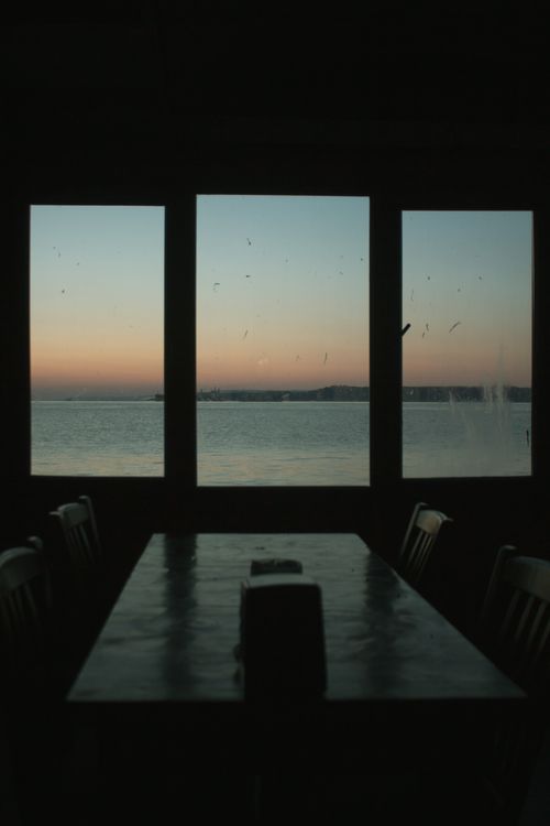Free Silhouette of chairs and table with a stunning sunset view of the sea through large windows. Stock Photo