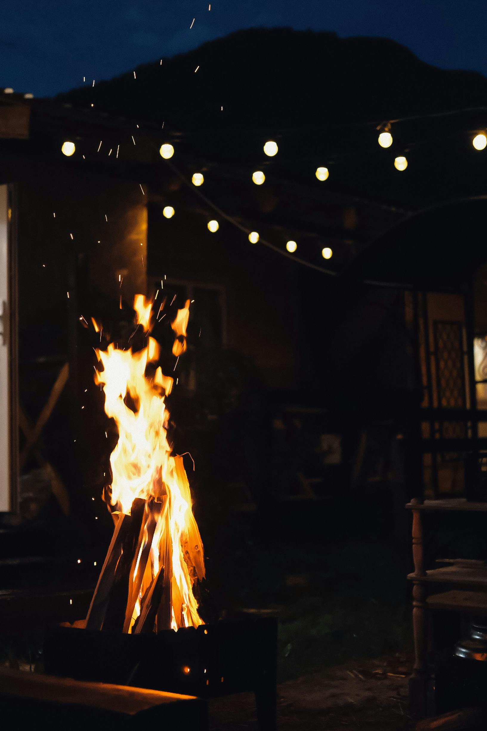 View of a Fire in a Fireplace Outside and String Lights at Night 