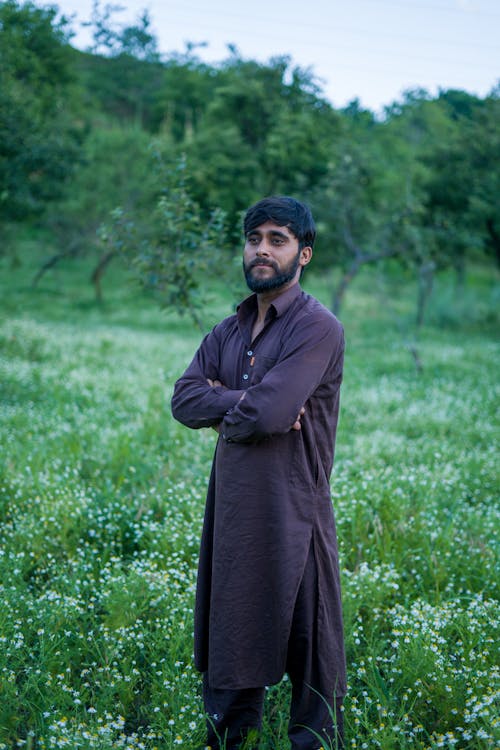 Man Wearing Traditional Clothing, Standing in a Green Field