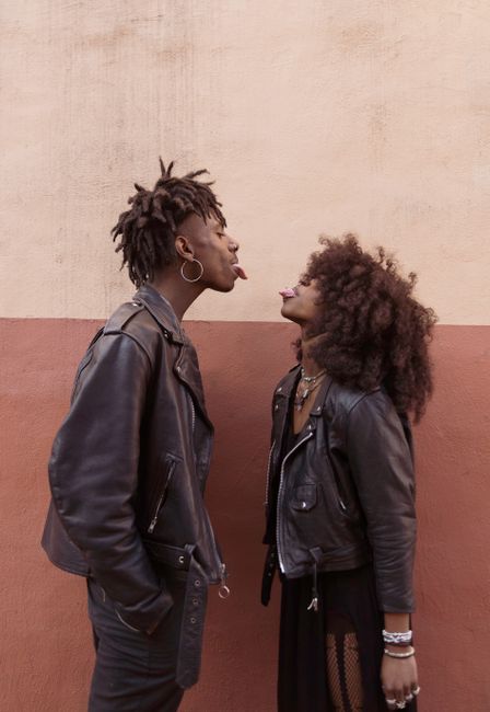 A couple shares a playful moment face to face, both wearing trendy leather jackets, expressing fun and humor.