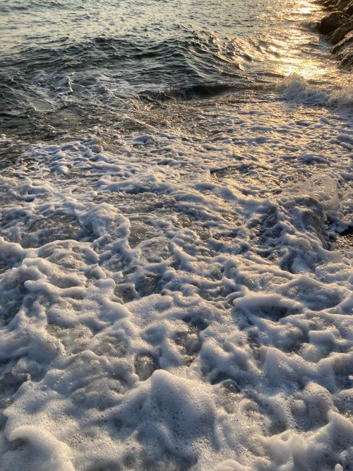 Free A serene view of ocean waves crashing on rocks with golden sunset reflections. Perfect for beach-themed designs. Stock Photo