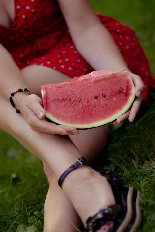 A woman in a red dress holding a slice of watermelon
