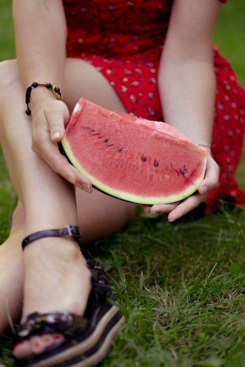 A woman in red shoes holding a slice of watermelon