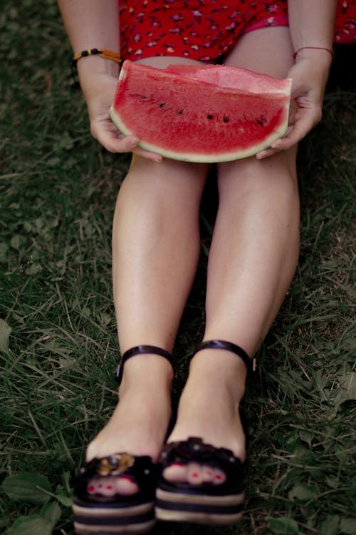 A woman in high heels holding a slice of watermelon