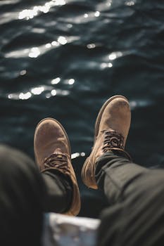 特写镜头中，破旧靴子悬挂在闪闪发光的水面上，捕捉到休闲的户外氛围