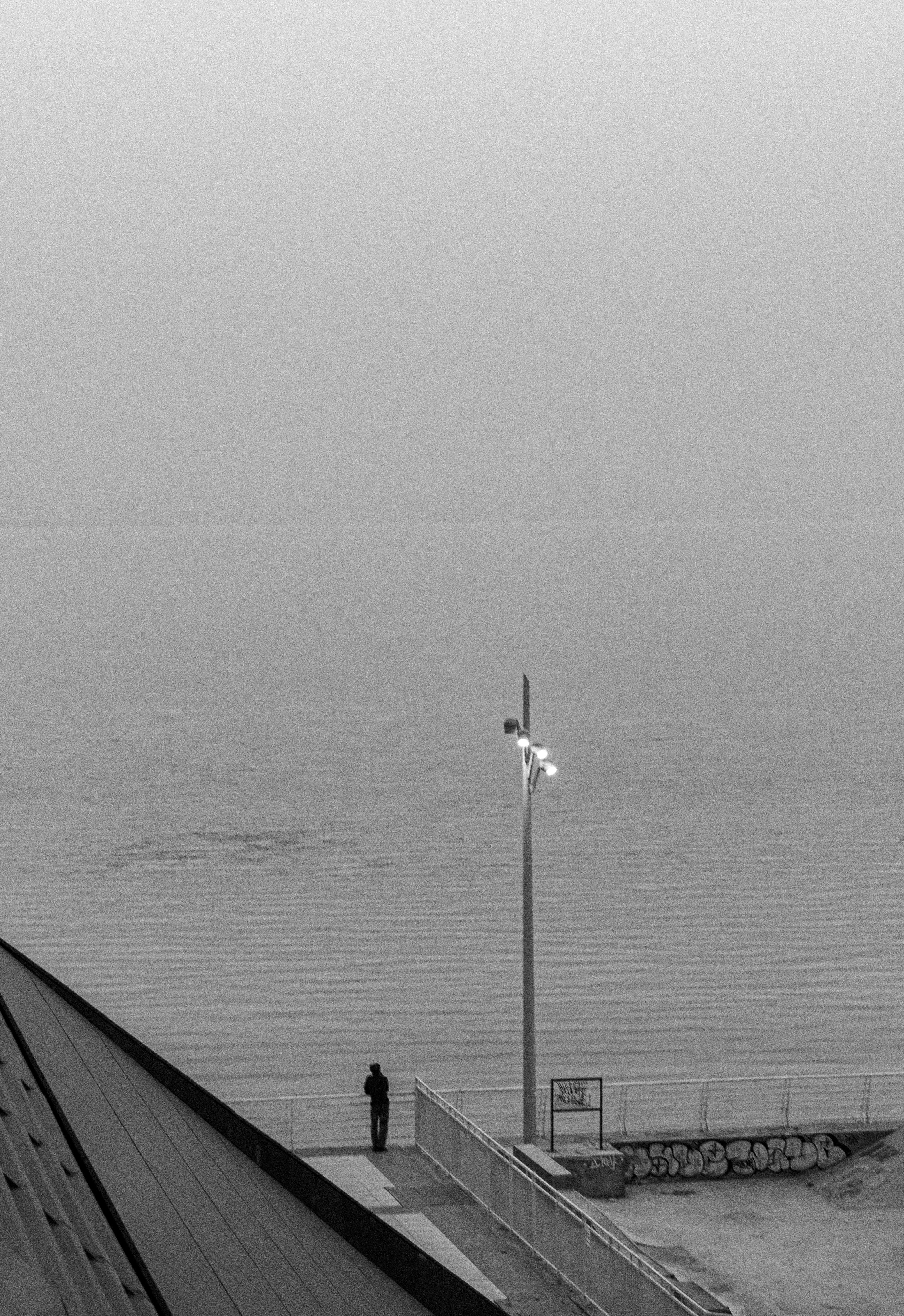 A tranquil black and white coastal scene with a lone figure by the sea on a foggy day.