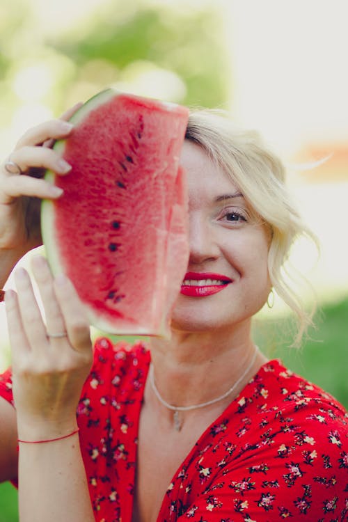 A woman holding up a piece of watermelon in front of her face