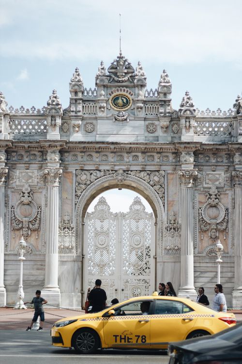 Free A vibrant yellow taxi passes in front of the ornate Dolmabahçe Palace gate in Istanbul, Turkey. Stock Photo