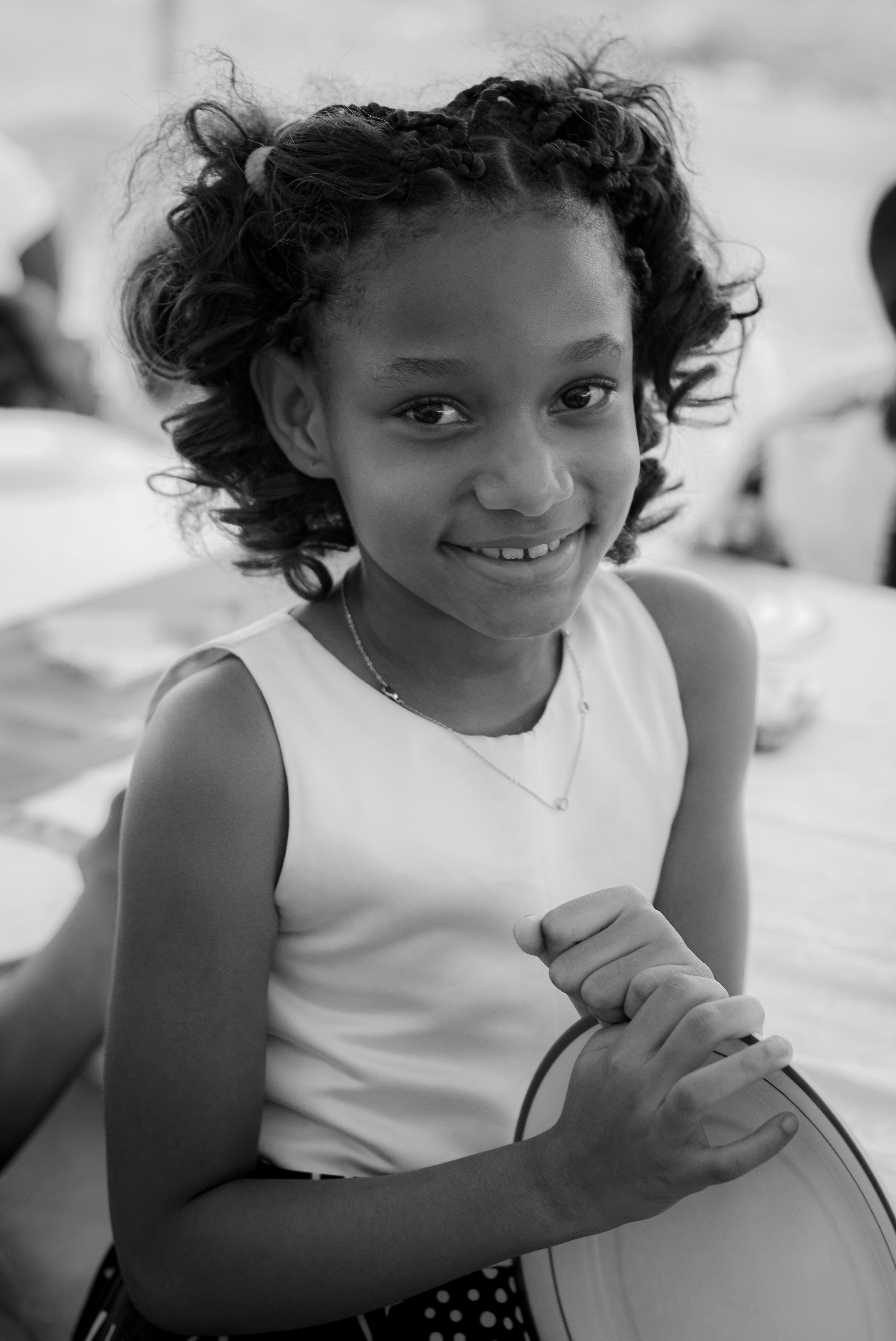 A joyful black and white portrait of a young girl smiling while outdoors in the daytime.