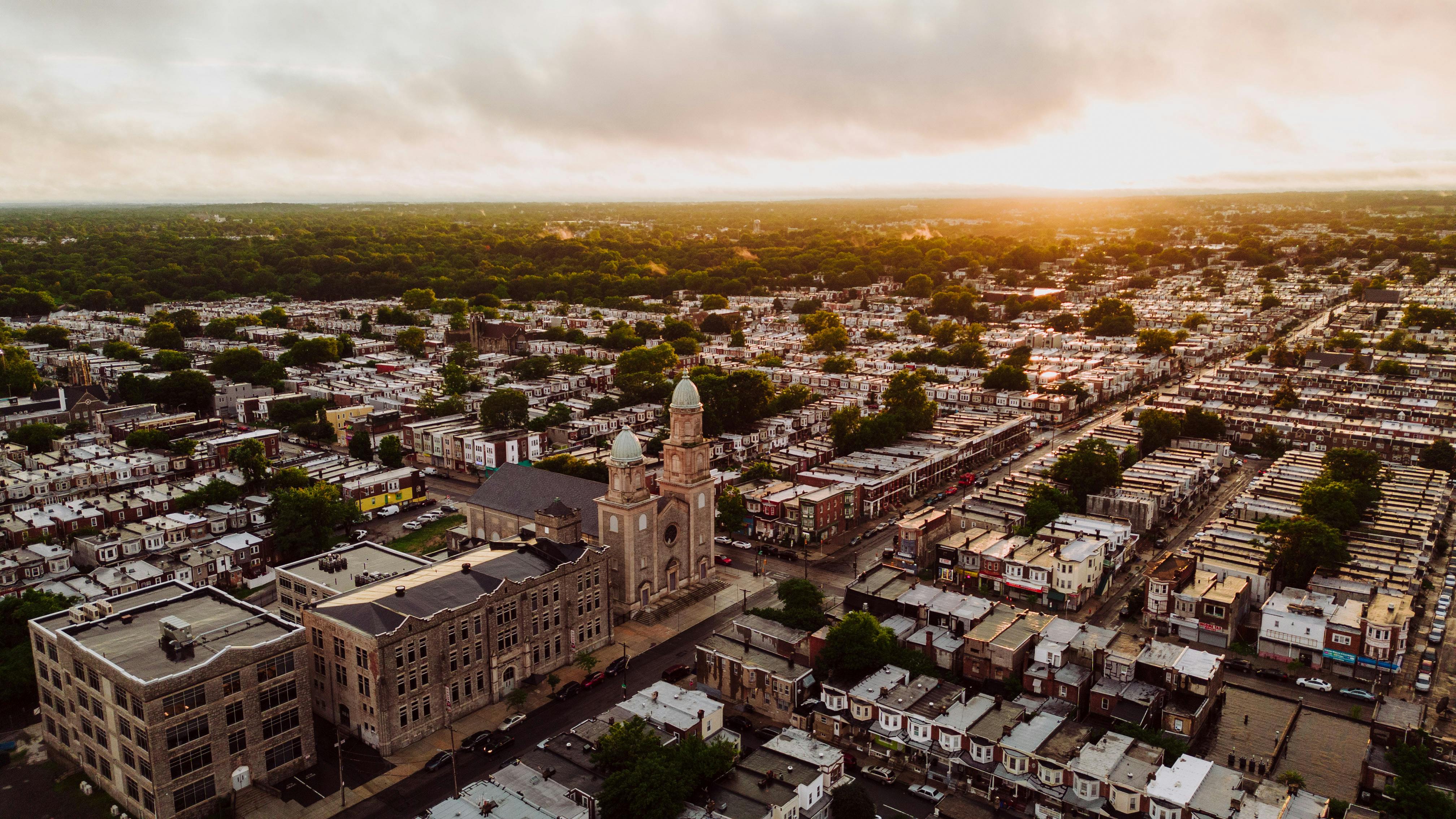 Drone shot of a Philadelphia church and neighborhood at sunset, showcasing urban architecture and green spaces.