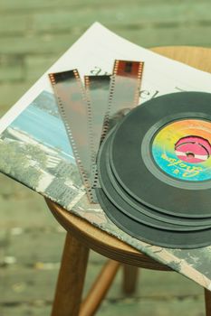 Vintage-themed image featuring vinyl records and film strips laid on a wooden chair.