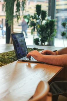 Hands typing on a laptop in a stylish, plant-filled indoor setting, capturing a modern work environment.