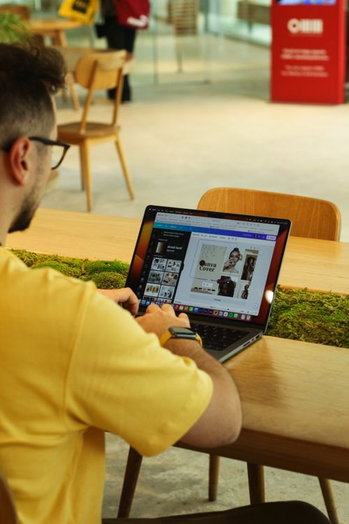 Free A man uses a laptop in a modern cafeteria, focusing on design work. Stock Photo