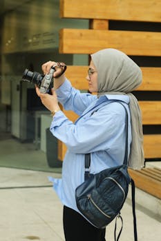 Side profile of a woman wearing a hijab capturing images with a digital camera outdoors.