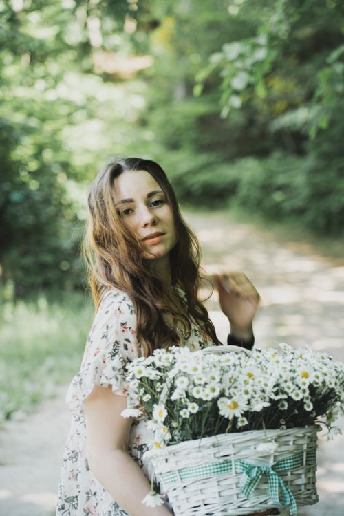 Free Young woman with long hair holding a white basket of wildflowers on a sunny day in nature. Stock Photo