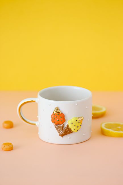 White mug with ice cream decoration against a vibrant yellow background, surrounded by lemon slices.