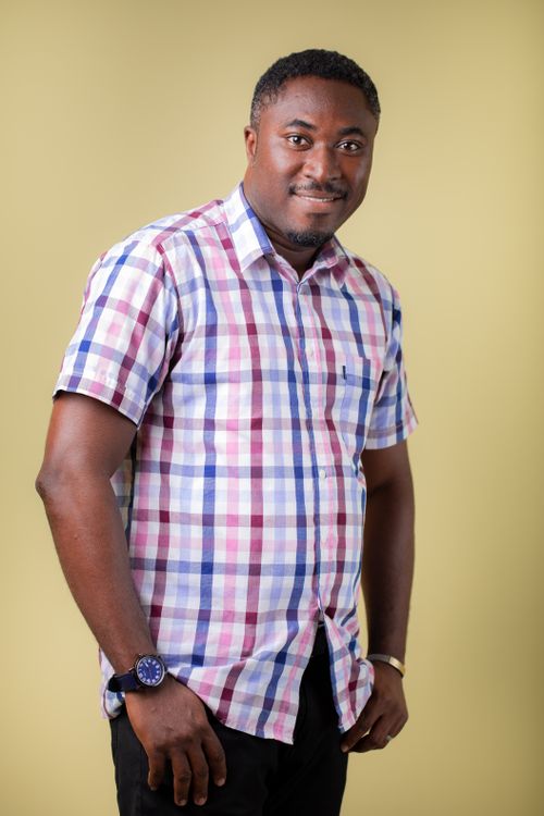 Free Portrait of a smiling man in a checkered shirt against a yellow background in Accra, Ghana. Stock Photo