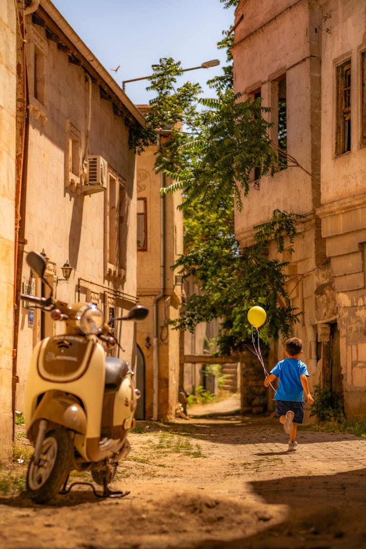 Boy Running With Yellow Balloon On Street In Old Town