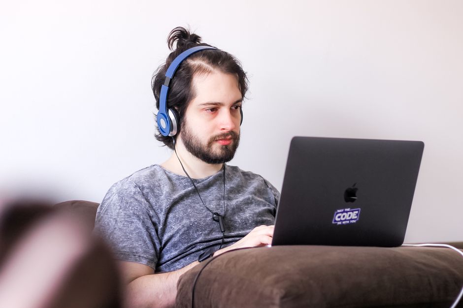A young man sitting on a couch using a laptop with headphones, working or studying remotely.