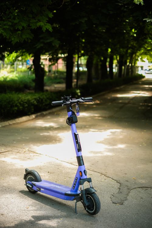 Free A purple electric scooter parked on a shaded park pathway on a sunny day. Stock Photo