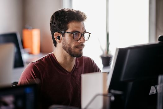 Man in eyeglasses concentrating on computer screen in modern office