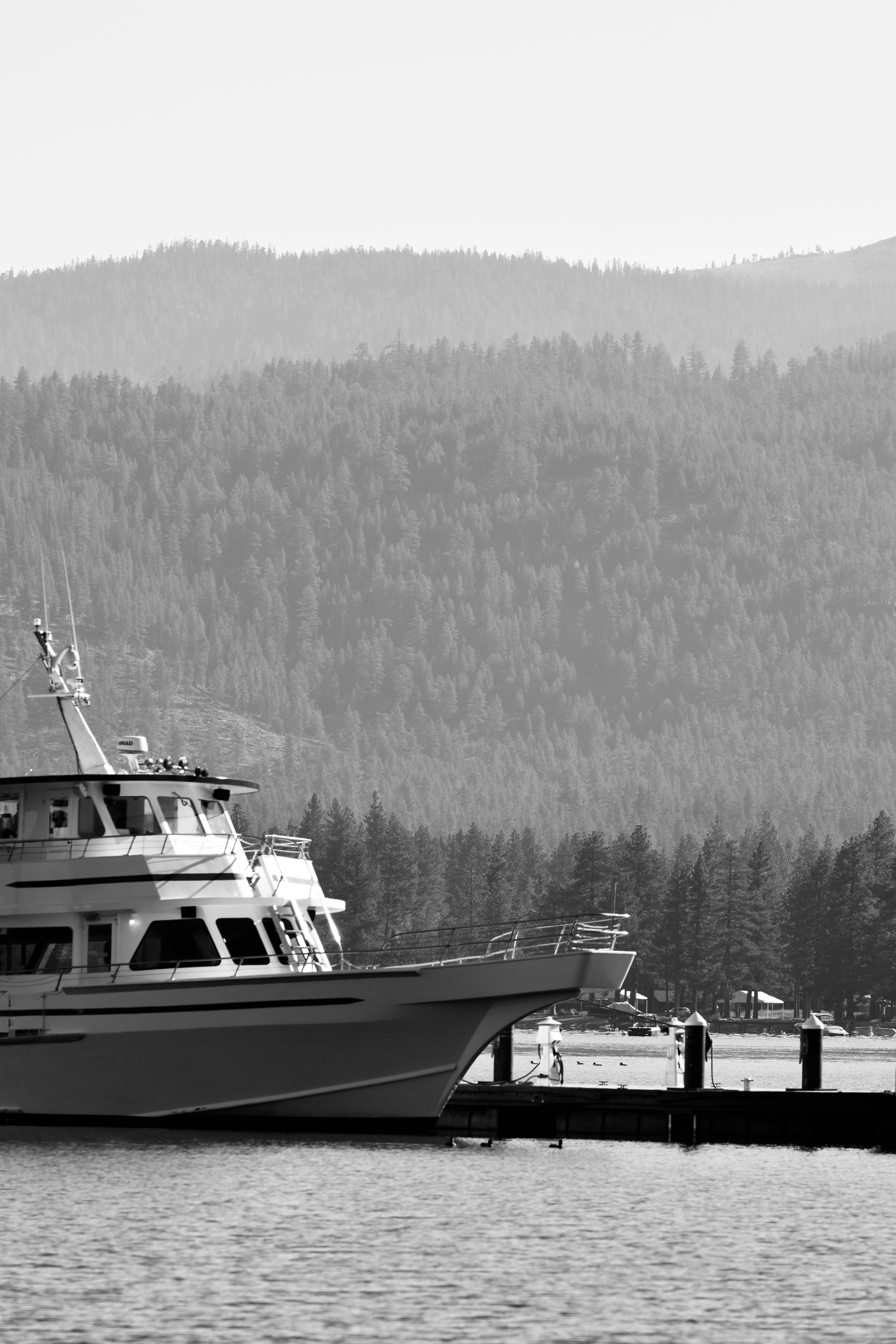 Black and white photo of a yacht moored near a mountain range pier in USA.