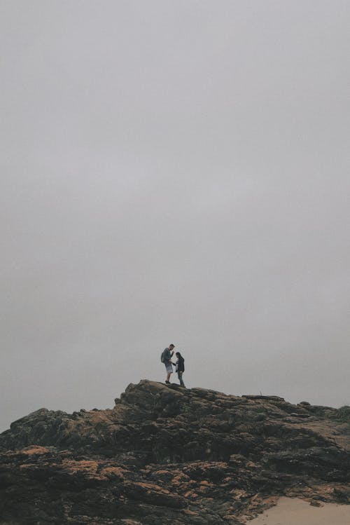 Man and Woman Standing on Rock Under White Sky