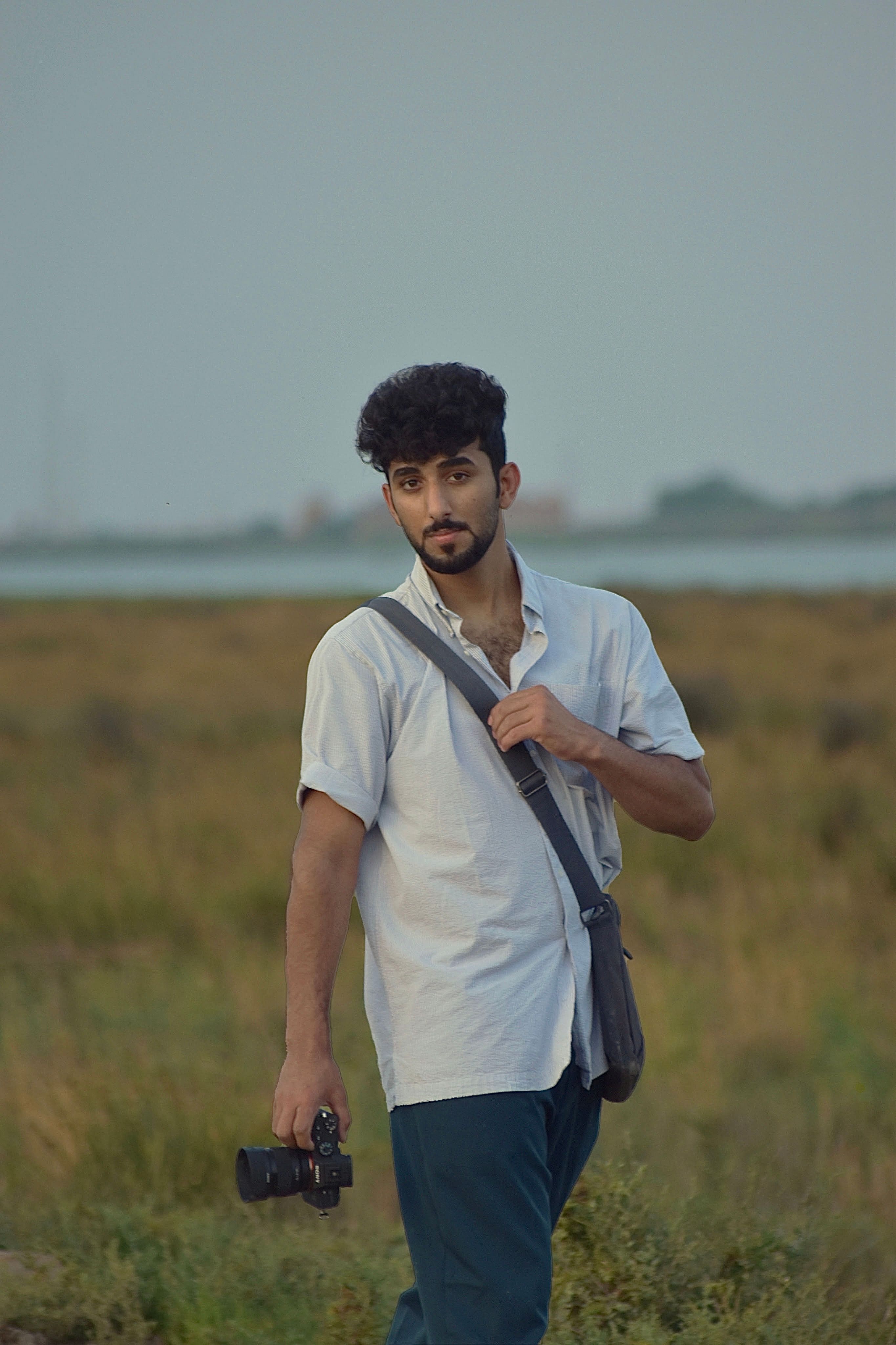 A young man holding a camera walks through a rural landscape, exuding a peaceful vibe.