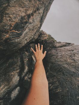 A close-up of a person's arm reaching toward rugged rocks outdoors, highlighting exploration.