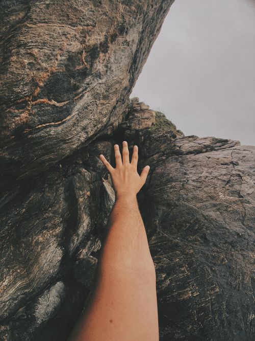 Free A close-up of a person's arm reaching toward rugged rocks outdoors, highlighting exploration. Stock Photo