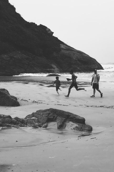 A family enjoys a playful run along a tranquil beach with rocky cliffs in the backdrop.