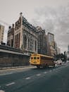 在城市场景中，一辆黄色校车在灰色天空下行驶于街道，背景是高楼大厦