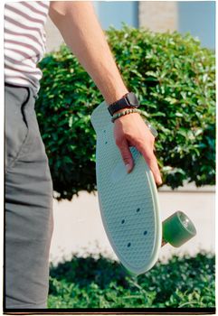 Side view of a young man holding a retro skateboard outdoors on a sunny day.