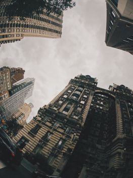 A dramatic low angle shot of urban skyscrapers with a cloudy sky, capturing modern and historic architecture.